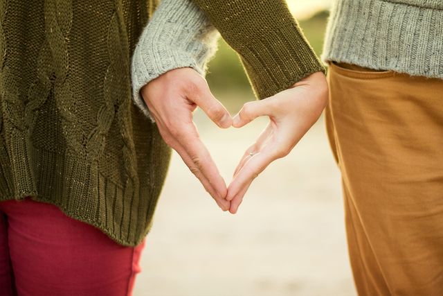 Image depicts two people, likely a couple, forming a heart shape together with their hands. They are wearing cozy sweaters and standing close to each other, implying a loving and intimate connection. This image can be used for Valentine's Day promotions, romantic blogs, relationship counseling advertisements, social media posts celebrating love, or any content focusing on love, affection, and togetherness.
