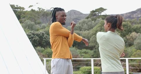 African American Man and Indian Woman Stretching on Outdoor Deck Overlooking Green Hills