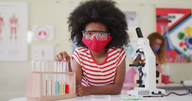 Young Black girl with goggles and mask conducting experiments in a science lab. Ideal for educational content, STEM programs, children's learning resources, science awareness campaigns and class materials.