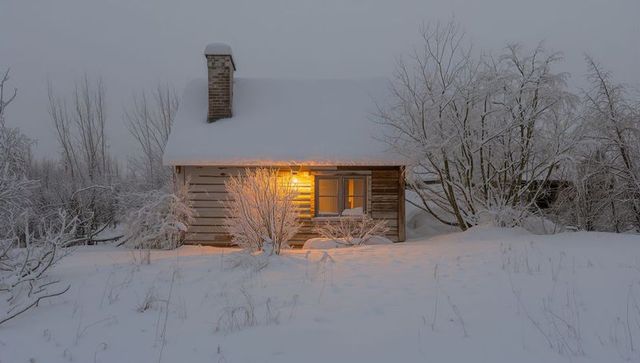 Snow-covered log cabin nestled in winter woods with warm glowing window