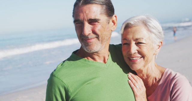 Senior couple smiling and embracing on a sunny beach day. Used for promoting senior lifestyle, retirement communities, vacation packages, or health and wellness for elders. Ideal for brochures, websites, advertisements aimed at the retired generation or elder care.