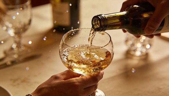 Elegant white wine pouring into coupe glass with sparkling bubbles and warm bokeh