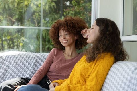 Smiling diverse friends relaxing on houndstooth sofa by sunlit window with green view