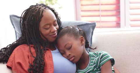 African american mother cuddling sleeping daughter on sofa conveying warmth, care and comfort