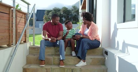 African american family sitting on steps talking, son gesturing during warm porch chat