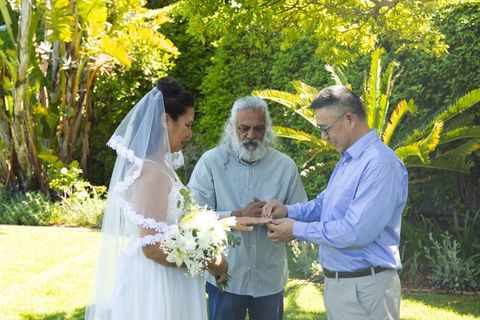 Outdoor garden wedding ceremony with indian officiant exchanging rings in sunlit moment