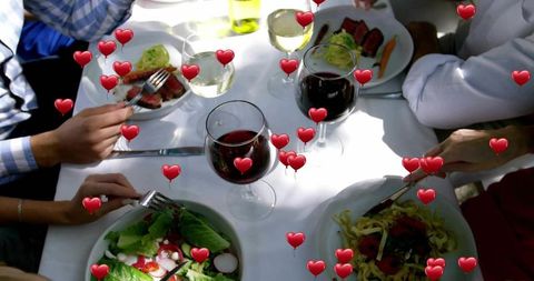 Friends sharing alfresco dinner with steak, wine and heart emojis on white tablecloth