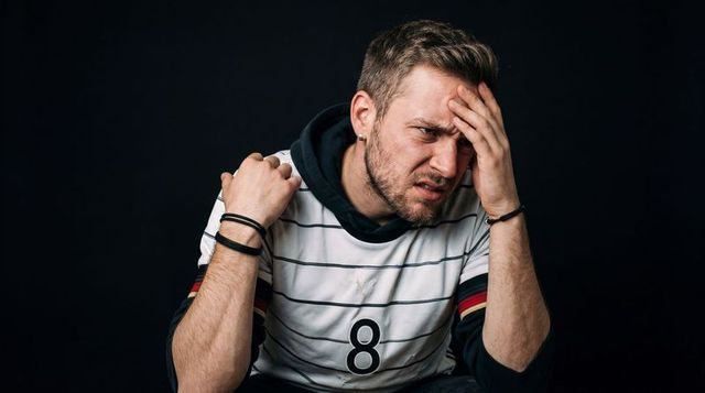Young man holding head and wincing, showing stress, pain and frustration