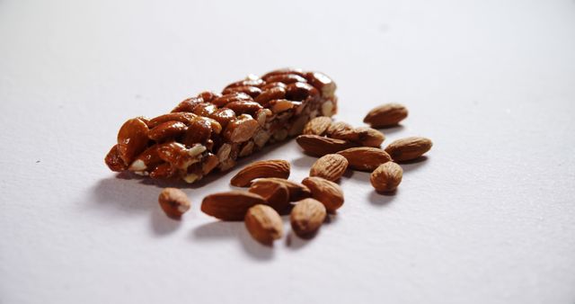 A bar of almonds is surrounded by scattered almond nuts on a white surface, with copy space. Almonds are a nutritious snack rich in healthy fats, protein, and fiber, often included in health-conscious diets.