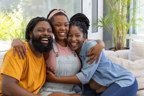 African family smiling and hugging on sofa in sunlit living room, joyful cozy togetherness