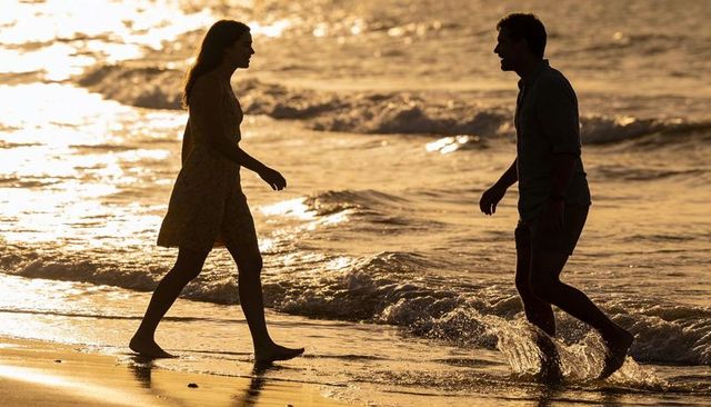 Walking and wading silhouetted couple on golden beach at sunset with reflected waves