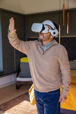 Middle-aged man using vr headset in cozy modern bedroom with mustard blanket and copper lights