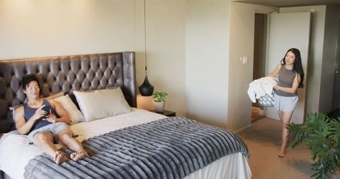 Asian couple relaxing in cozy minimalist master bedroom with tufted headboard and plants