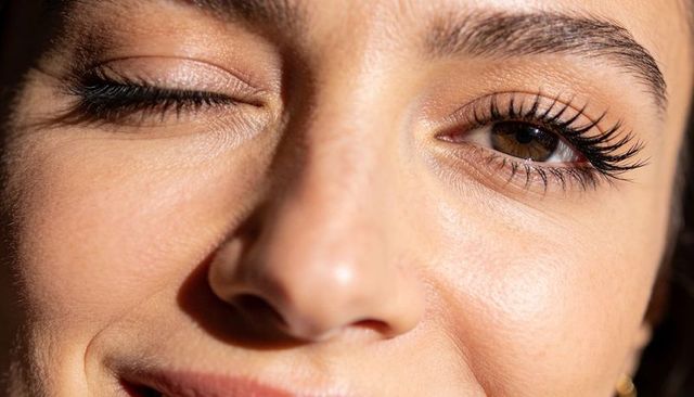 Winking female closeup showing long lashes, mascara and natural skin texture in warm light