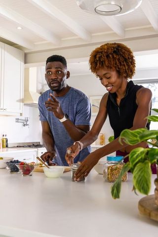 Black couple making healthy breakfast together in light-filled modern kitchen