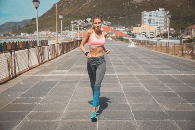Caucasian woman running on a seaside promenade, showcasing an active and healthy lifestyle. Ideal for promoting fitness, outdoor exercise, summer activities, and urban coastal living. Perfect for use in health and wellness campaigns, sportswear advertisements, and travel brochures.
