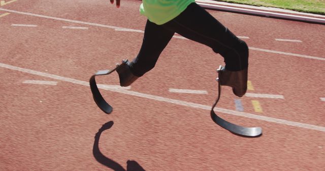 Person running on track with prosthetic legs demonstrating determination in sports. Useful for articles on overcoming challenges, sports for disabled individuals, fitness, and inspiring athletic stories.