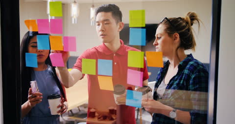 Diverse Team Collaborating on Glass Board with Sticky Notes