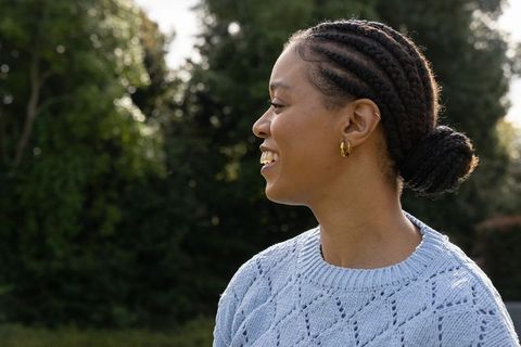 African american woman standing in park wearing light blue sweater smiling in rim light
