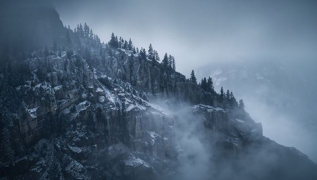 Misty alpine ridge with snow-dusted cliffs and pine silhouettes in foggy mountain valley