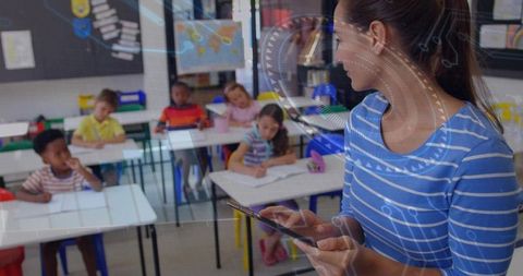 Female teacher using tablet while teaching elementary classroom with diverse students