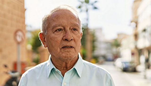Senior man standing on sunlit urban street squinting and reflecting in warm natural light