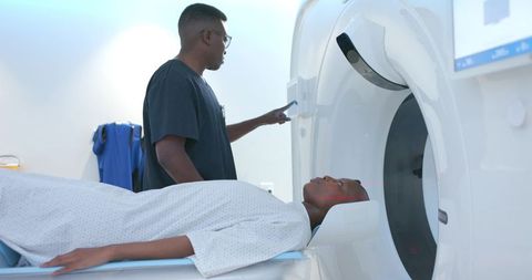 African radiologic technologist operating ct scanner while female patient lying on table