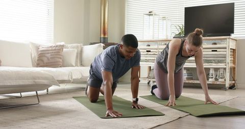 Couple practicing floor core exercise on yoga mats in bright living room