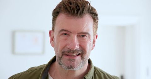 Mature man smiling confidently at home in olive green shirt