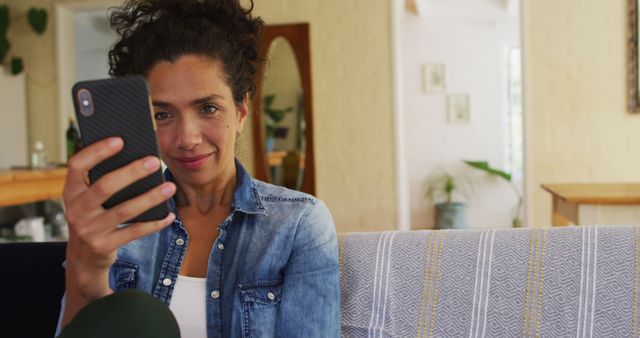 Caucasian woman using smartphone on image call, sitting on sofa at home. Staying at home in self isolation during quarantine lockdown.