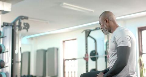 Senior african american man resting on gym bench after strength training, focused and calm