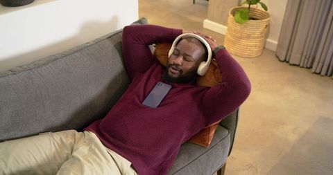 African American man relaxing on sofa listening to music with headphones, home interior