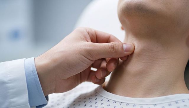 Clinician palpating thyroid on patient neck during physical exam