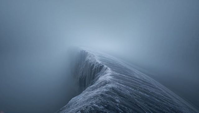 Icy glacier ridge vanishing into dense fog, frozen crevasse and cold blue landscape