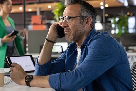 Middle-aged professional talking on phone in modern open office while working on tablet