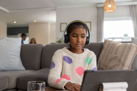 Indian daughter using tablet with headphones in cozy living room family technology scene