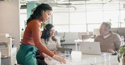 Team Collaborating Around Bright Open-Plan Table With Woman Arranging Documents and Laptop