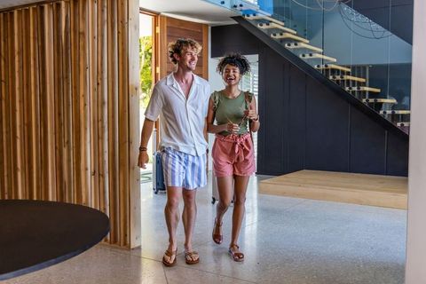 Young couple arriving at modern vacation rental carrying luggage and smiling in entryway