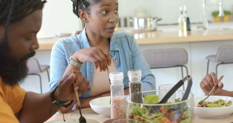 Family sharing casual kitchen dinner with young woman talking and fresh salad bowl