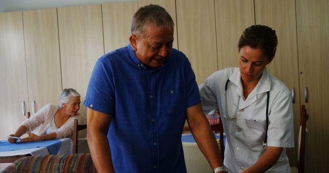 Nurse assisting an elderly man to stand up within a nursing home, showcasing quality care and support. In background, another senior woman is using a phone, highlighting the integration of modern technology in care facilities. Useful for themes involving elderly care, healthcare services, nursing professions, and promoting family discussions on aged care.