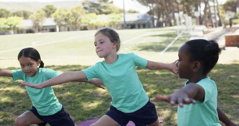 School girls practicing outdoor yoga for teamwork and balance in green tees and navy shorts