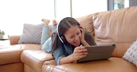 Girl enthusiastically engaged with tablet and headphones on couch