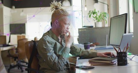 Focused coworking professional typing at dual-screen desk with laptop, notebooks and coffee
