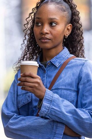 African american woman in 20s holding coffee cup wearing denim jacket urban portrait