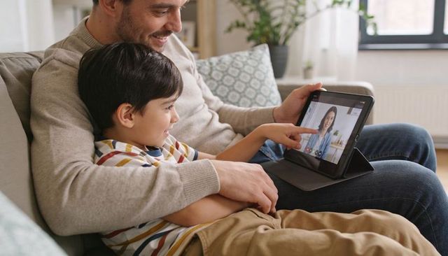 Smiling father and son having video call on tablet while cuddling on couch