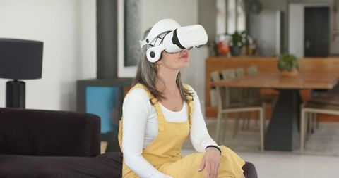 Mature woman exploring virtual reality at home with white VR headset and mustard overalls