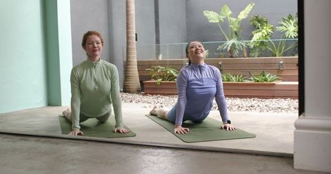 Two women practicing yoga on courtyard mats, stretching into upward cobra pose, smiling