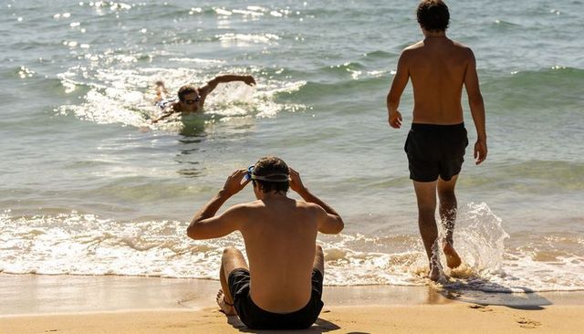 Young men adjusting goggles and entering ocean for open-water swim on sunny sandy beach
