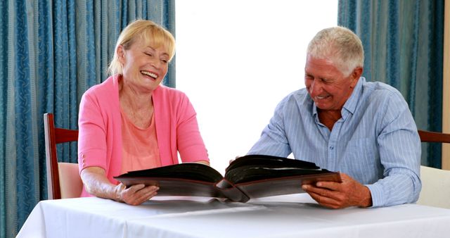 Senior couple enjoying time reminiscing with a photo album, showing happiness and bonding. Ideal for topics related to aging, family memories, relationships, and retirement. Perfect for use in ads, articles on elderly care or marketing campaigns focusing on older adult happiness and nostalgia.
