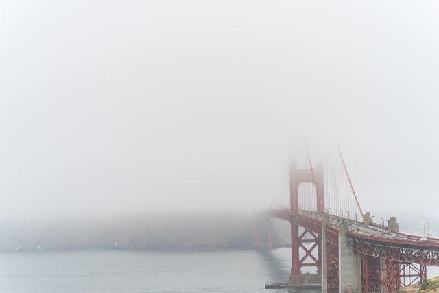 Golden Gate Bridge partially covered in thick fog creates mysterious and iconic view. Suitable for travel blogs, weather updates, San Francisco tourism promotion, and illustrating atmospheric conditions.